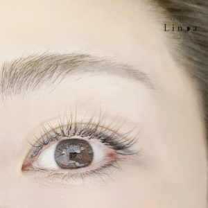 カラーマツエク（ブラウン×アクアマリンMIX）。ブラウンベースに少量のアクアマリンを加えて爽やかで抜け感のある仕上がりに。髪色や眉色と調和し、垢抜けた印象を演出する大人のカラーまつ毛デザイン