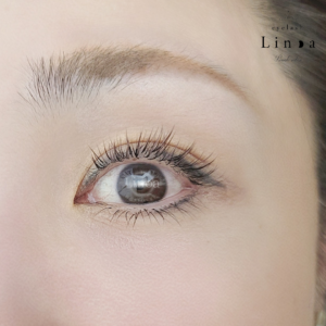 上下まつ毛にダークブラウンとスモーキーパープルをミックスしたカラーエクステ。アップワード仕上げで下向きまつ毛を自然に立ち上げ、下まつ毛は片目約15本でナチュラルに整えた上品な目元デザイン。